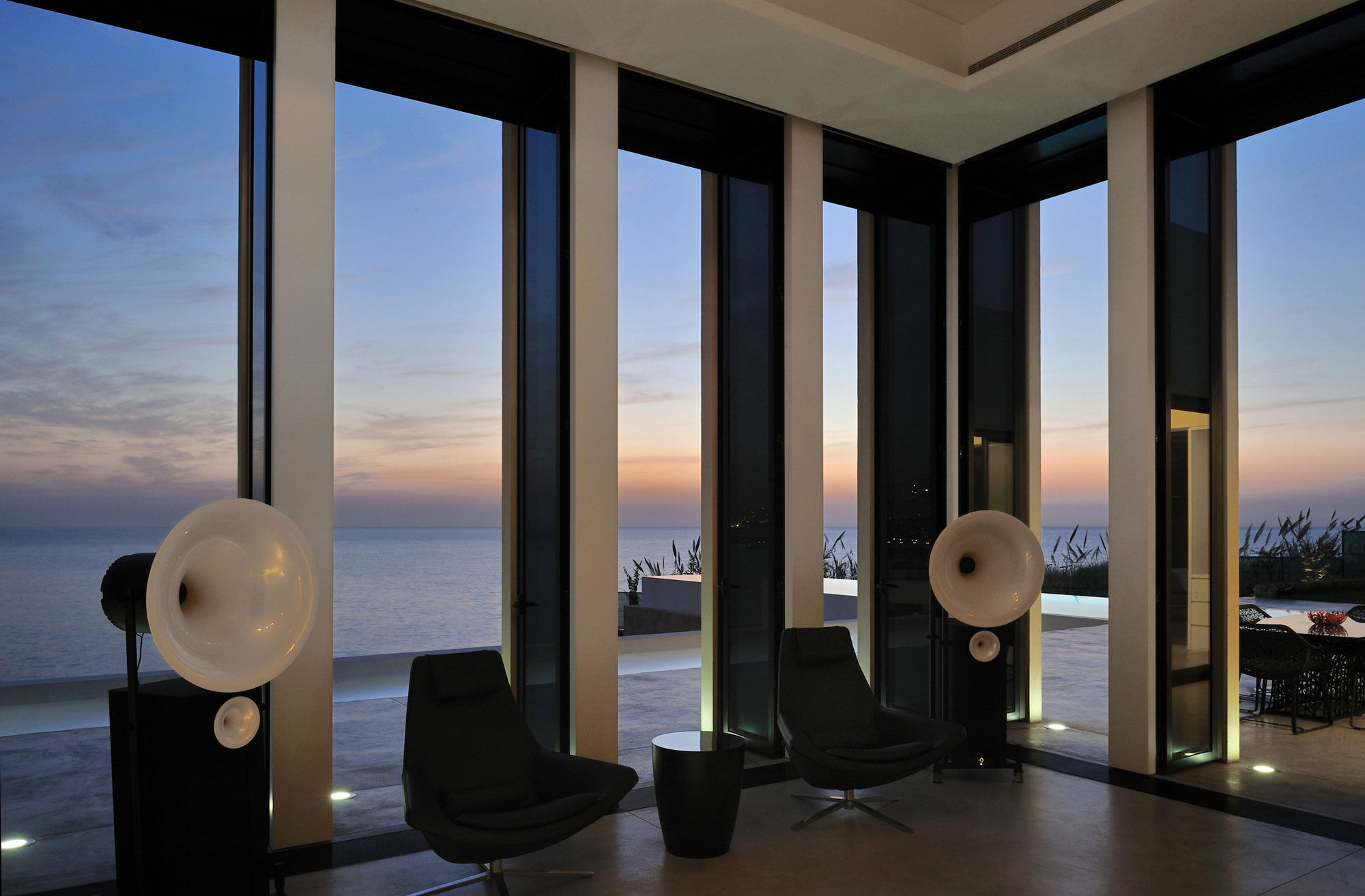 Beach And Sparkling Attractive Beach And Sunset View Sparkling Outdoor Lights Transparent Glass Wall Dark Glove Chairs Sleek Dark Stool Fidar Beach House Dream Homes  Futuristic Modern Beach House With Neutral Color Palettes For A Family Of Five