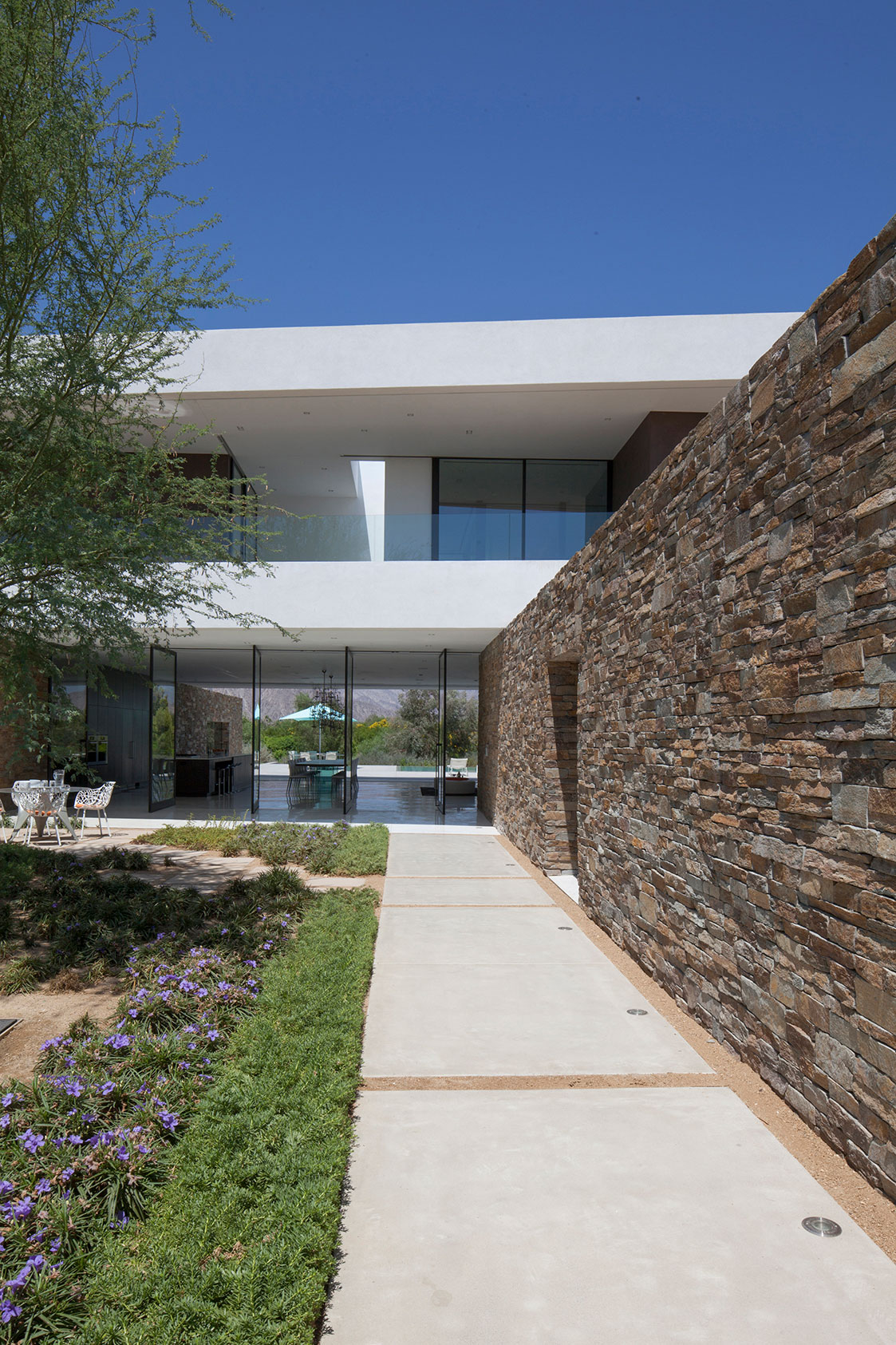 Stone Wall Colorful Rough Stone Wall Concrete Path Colorful Flowers On Modern Garden Glass Door White Chairs Open Plan Interior In Madison House Dream Homes Spectacular And Spacious Contemporary House With Sliding Glass Walls